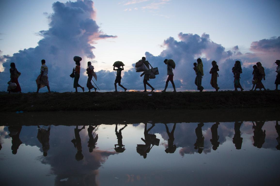 Silhouette of refugees walking on horizon along river