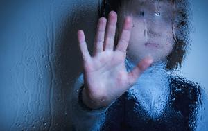 Sad child behind a glass wall. It touches the wall with the hand. Blue background.