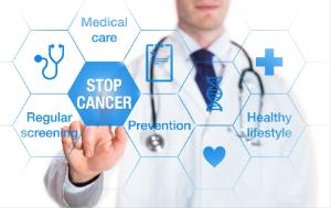 Man wearing a doctor’s white coat and with stethoscope around his neck pointing his finger to a sign with stop cancer; other signs read medical care, regular screening, prevention and healthy lifestyle