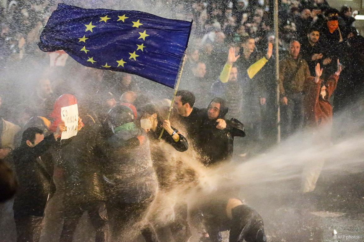 Protesters brandishing a European Union flag brace as they are sprayed by a water cannon during clashes with riot police near the Georgian parliament in Tbilisi on March 7, 2023.